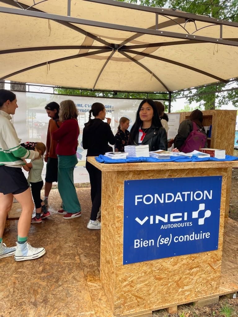 Stand de la Fondation VINCI Autoroutes, slogan « Bien (se) conduire », avec une personne derrière la table et des livres posés dessus