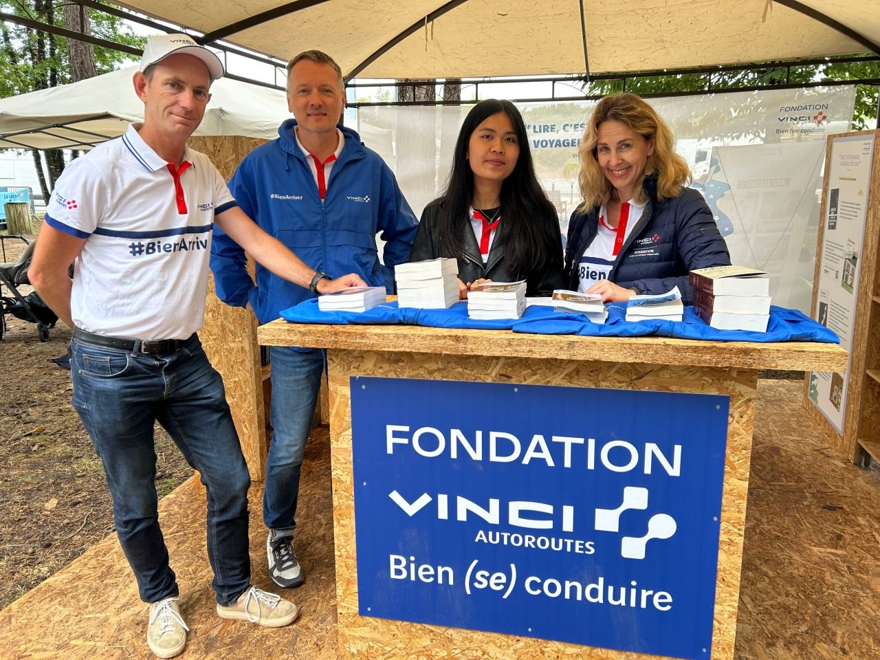 Quatre personnes devant le stand, avec la banderole « Lire, c'est voyager… » en arrière-plan
