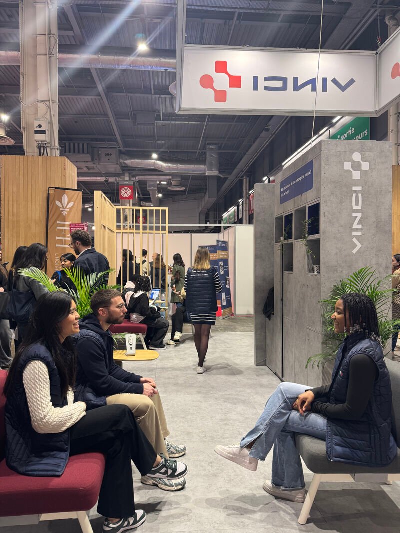 Espace d'accueil du stand VINCI, avec des personnes assises sur des canapés